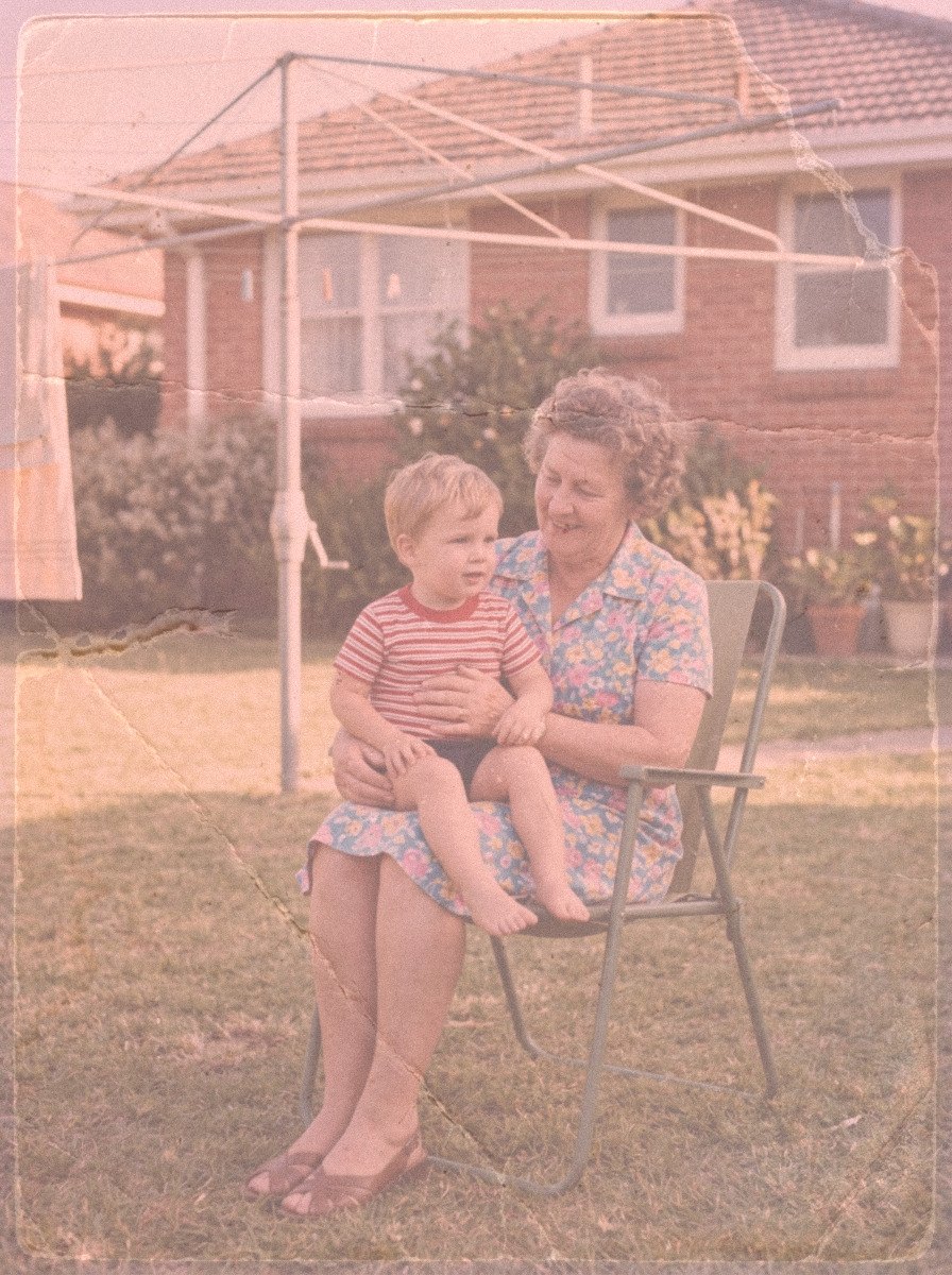 Heavily faded 1970s colour snapshot of a grandmother with a small boy on her knee, washed out with a strong colour cast