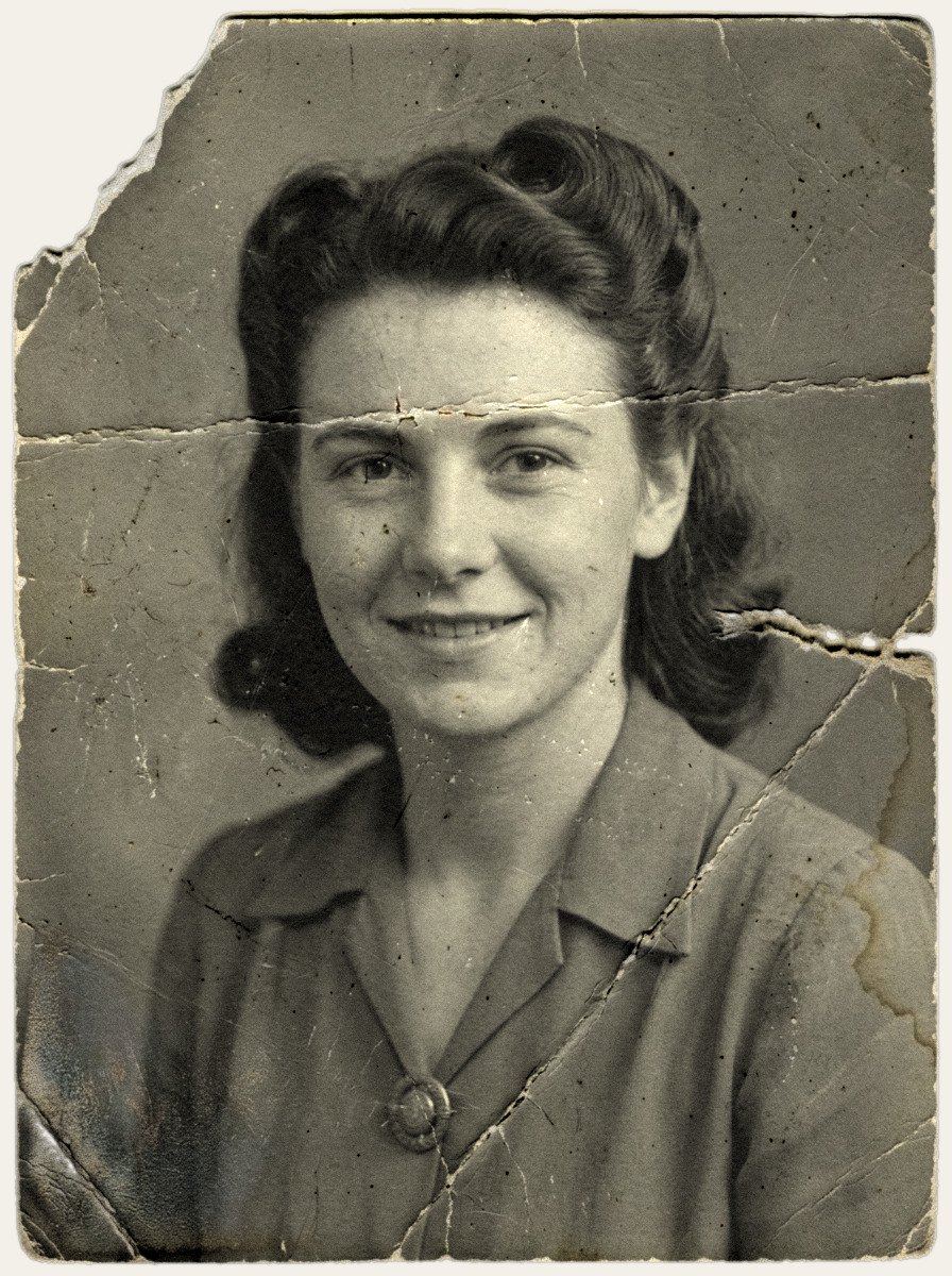 Damaged 1940s black-and-white studio portrait of a young woman with wavy hair, scratched and creased with a missing corner