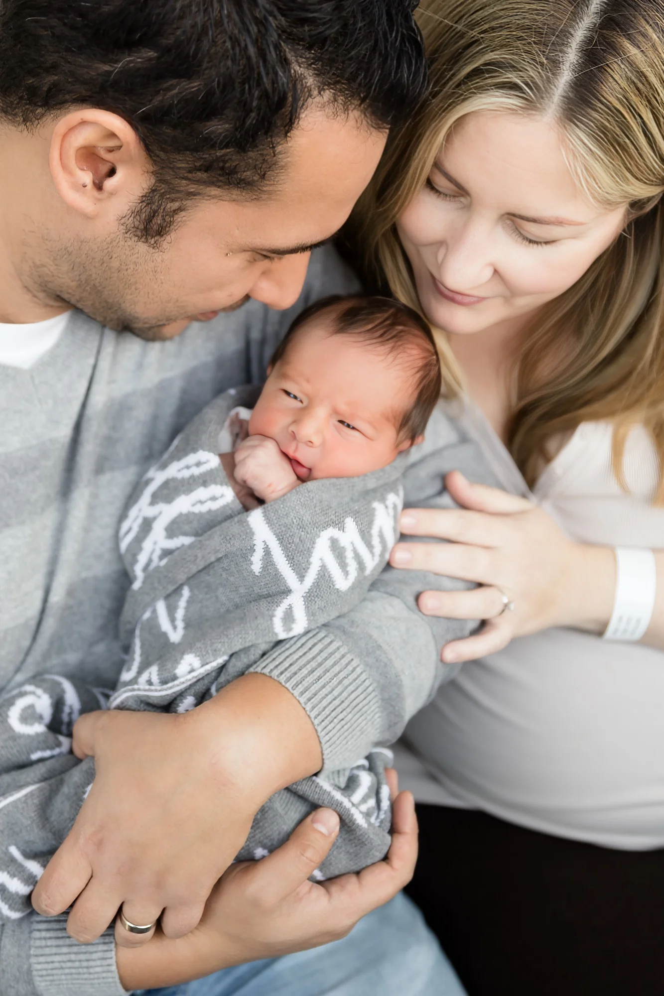 Parents holding their newborn at the hospital bedside, mum still wearing her wristband