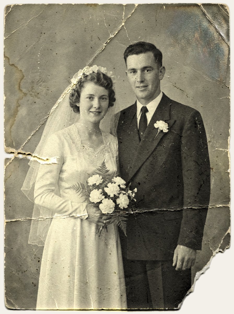 Damaged 1950s black-and-white wedding portrait of a bride and groom, faded with creases, scratches and a torn corner