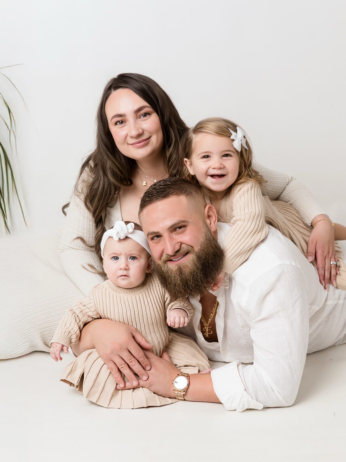 Mum, dad and two young daughters cuddling in beige and white outfits during a light studio family portrait session